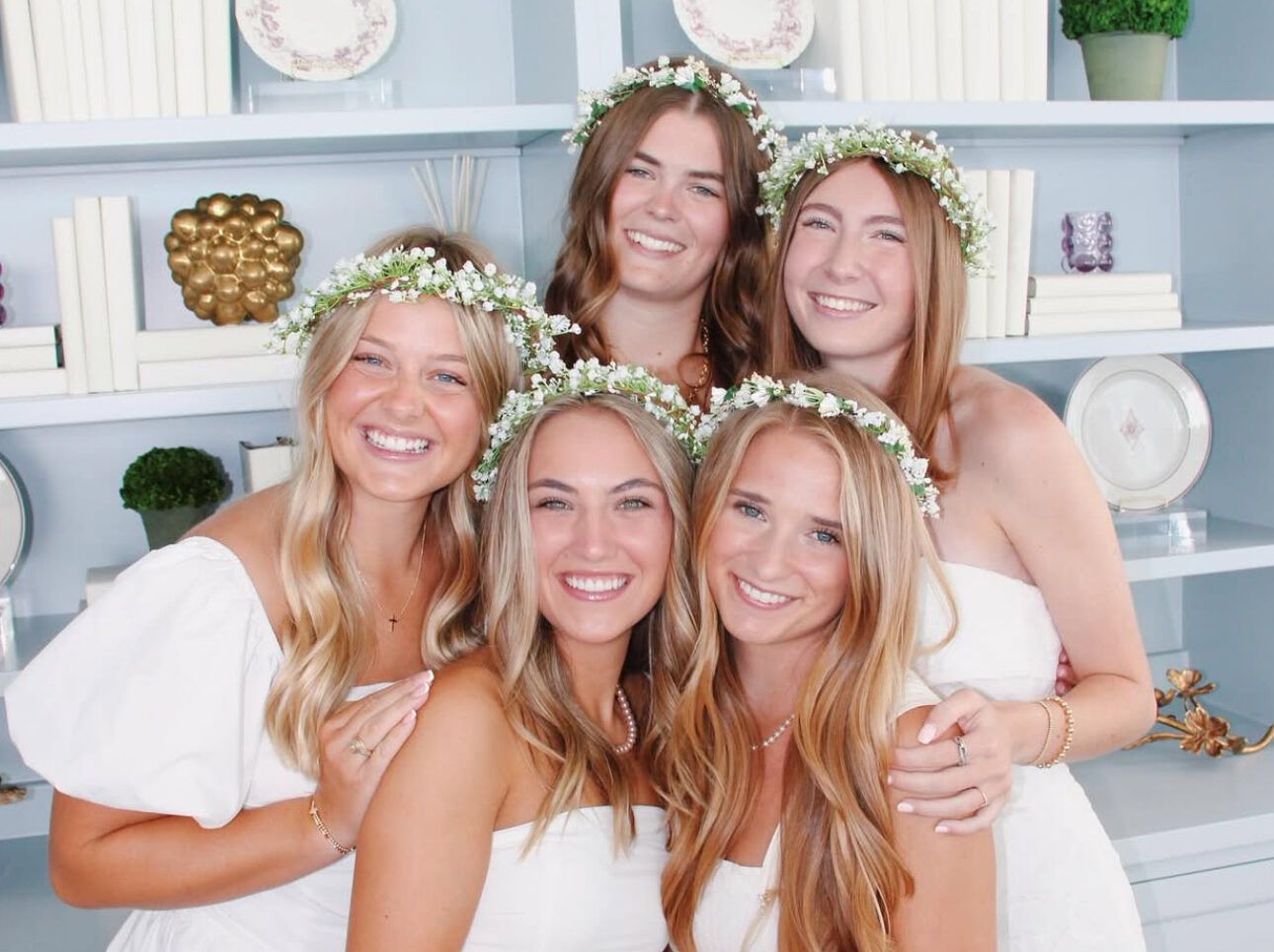 Five members wearing white dresses and flower crowns