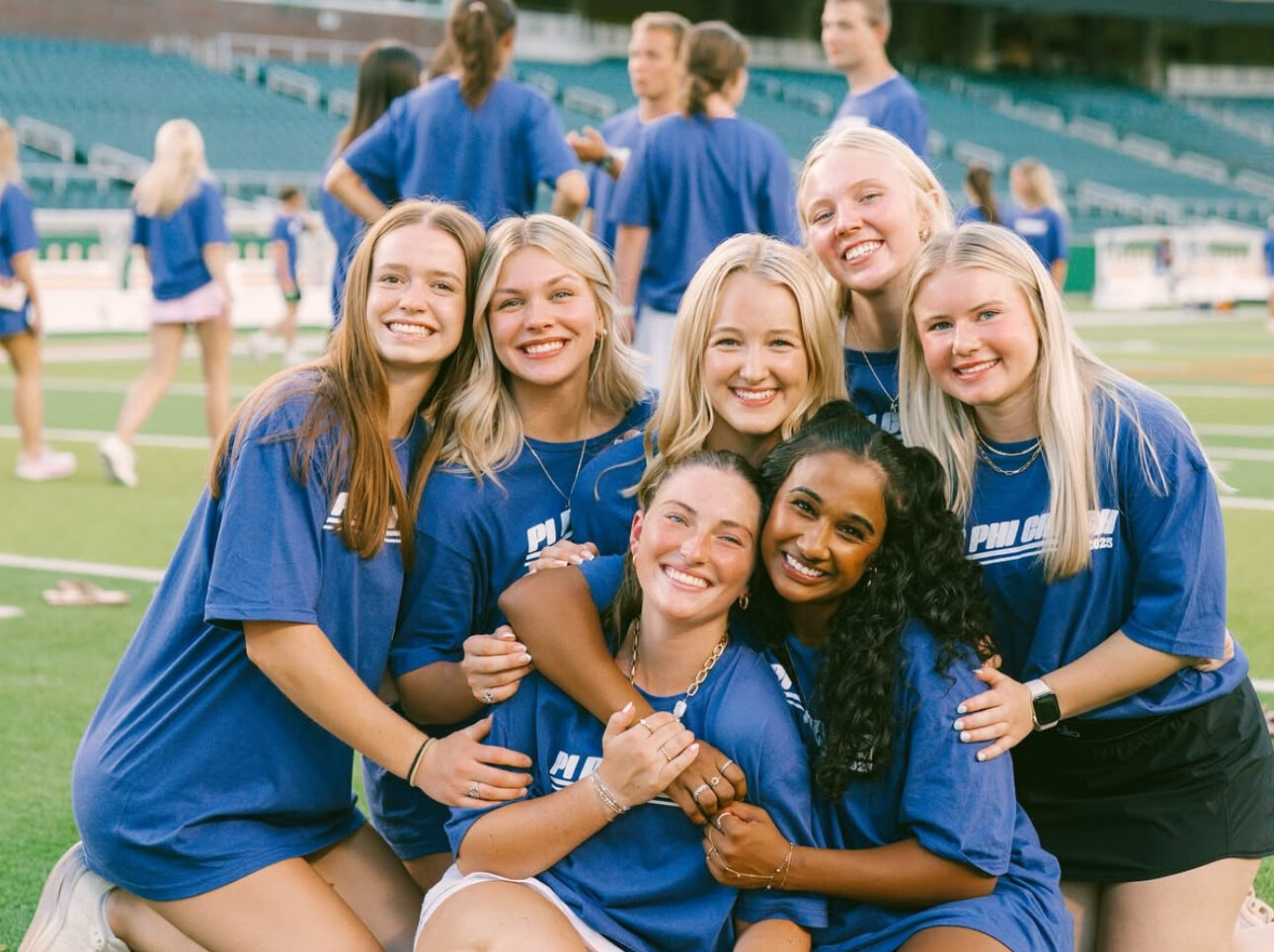 Seven members sitting on a football field hugging