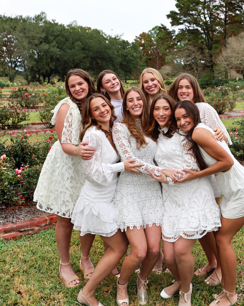 Eight individuals wearing white dresses in a grassy field