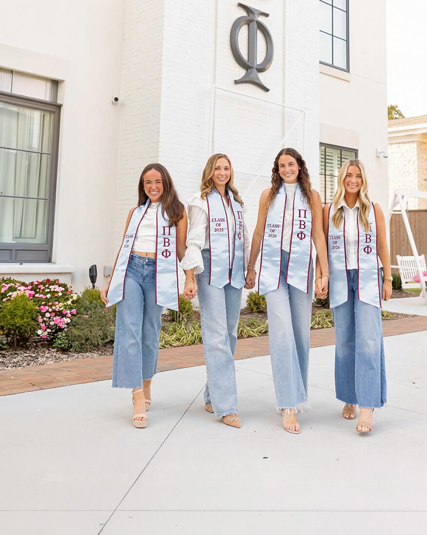 Four individuals wearing graduation stoles standing in front of a chapter house