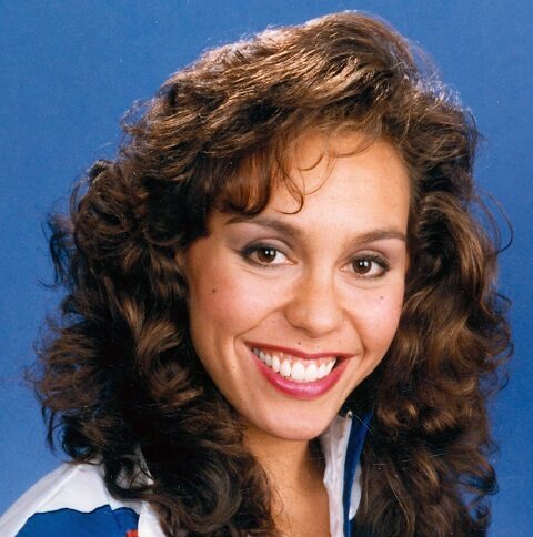 Professional headshot of Tracie Ruiz Conforto wearing a blue and white athletic jacket in front of a blue background