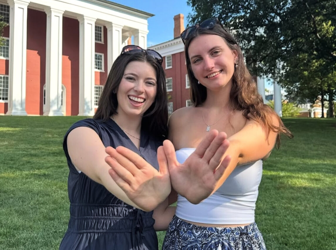 Two members making angel wings with their hands standing in front of a grass area