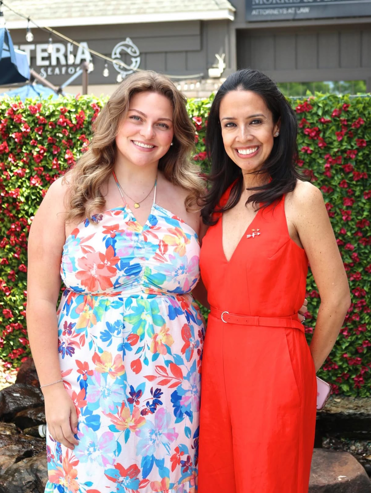 Two members standing outside in front of a greenery wall
