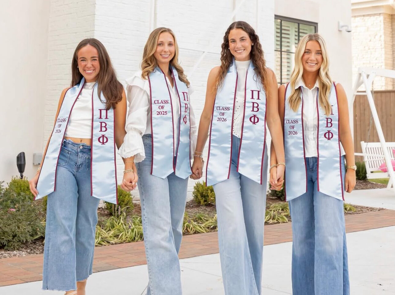 Four members wearing graduation stoles and standing in front of the chapter house