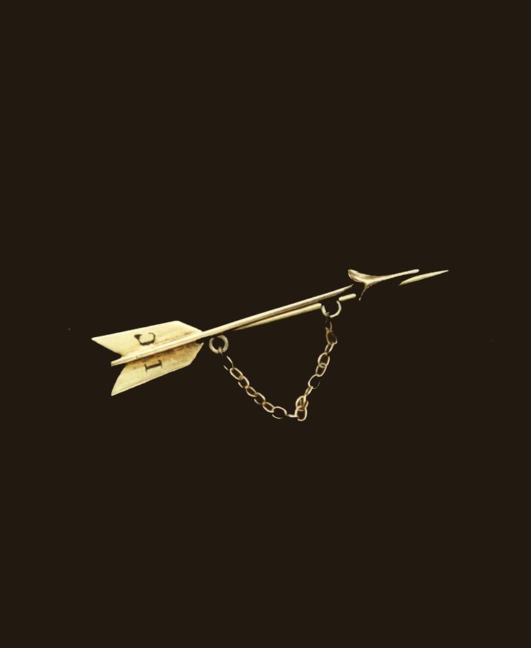 Close-up of a vintage Pi Beta Phi gold arrow pin with chain against a dark background
