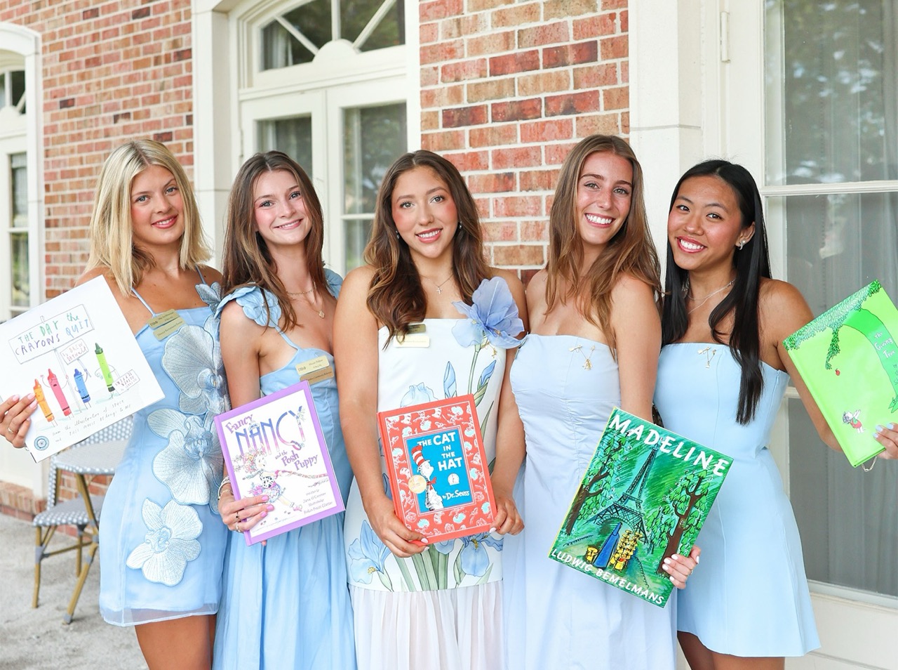 Image of five individuals standing outdoors holding children's books