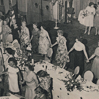 Pi Phis standing around a table holding hands while singing Pi Phi Grace